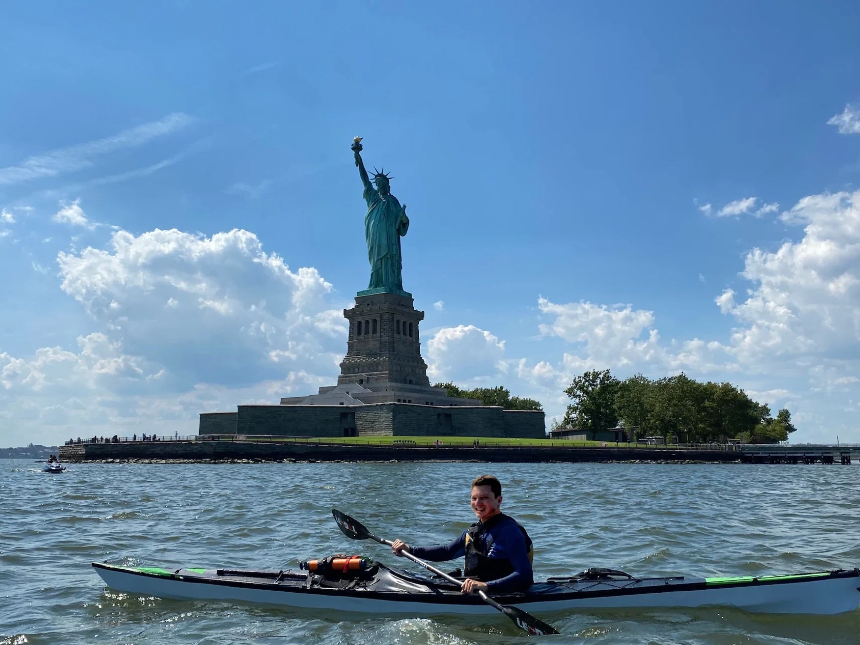 Man kayaking on a TRAK Kayak near the Statue of Liberty on a sunny day.
