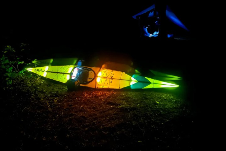 Illuminated kayak on ground at night with colorful lights, tent visible in the background.
