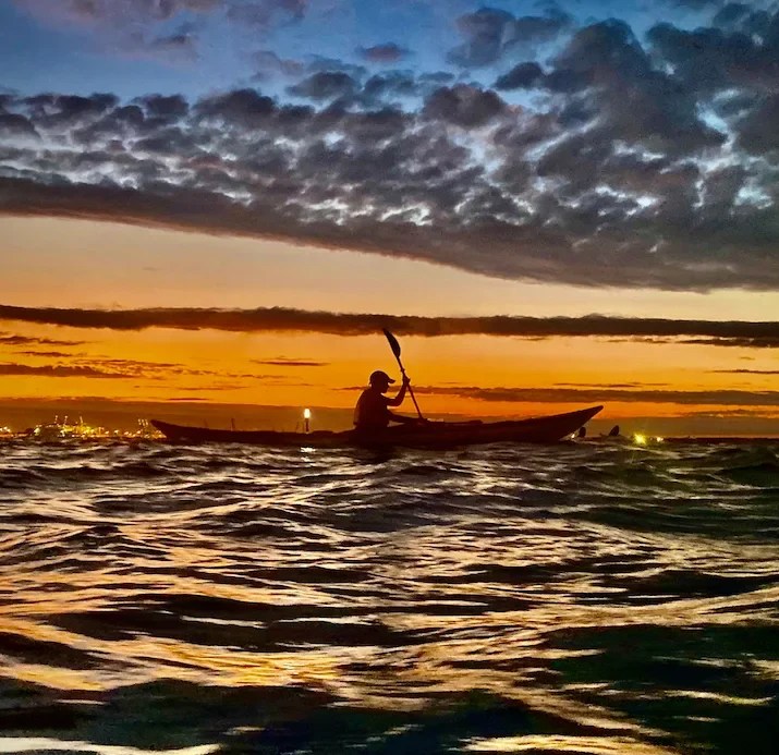 Silhouette of a person kayaking on the Upper New York Bay during sunset with dramatic clouds.