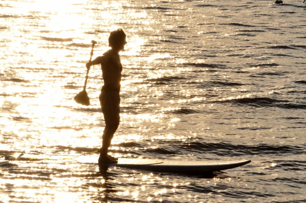 Silhouette of person paddleboarding on water with sunlight reflections.