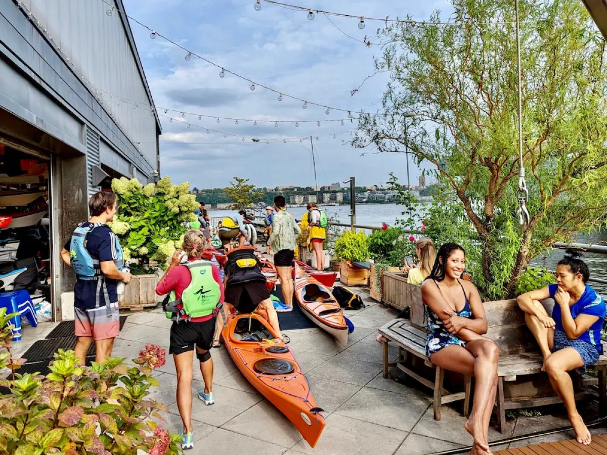 People preparing kayaks by a riverside with some seated nearby.
