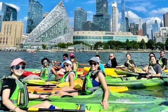 Beginner group kayaking on the Hudson River with city skyline and modern architecture in background.