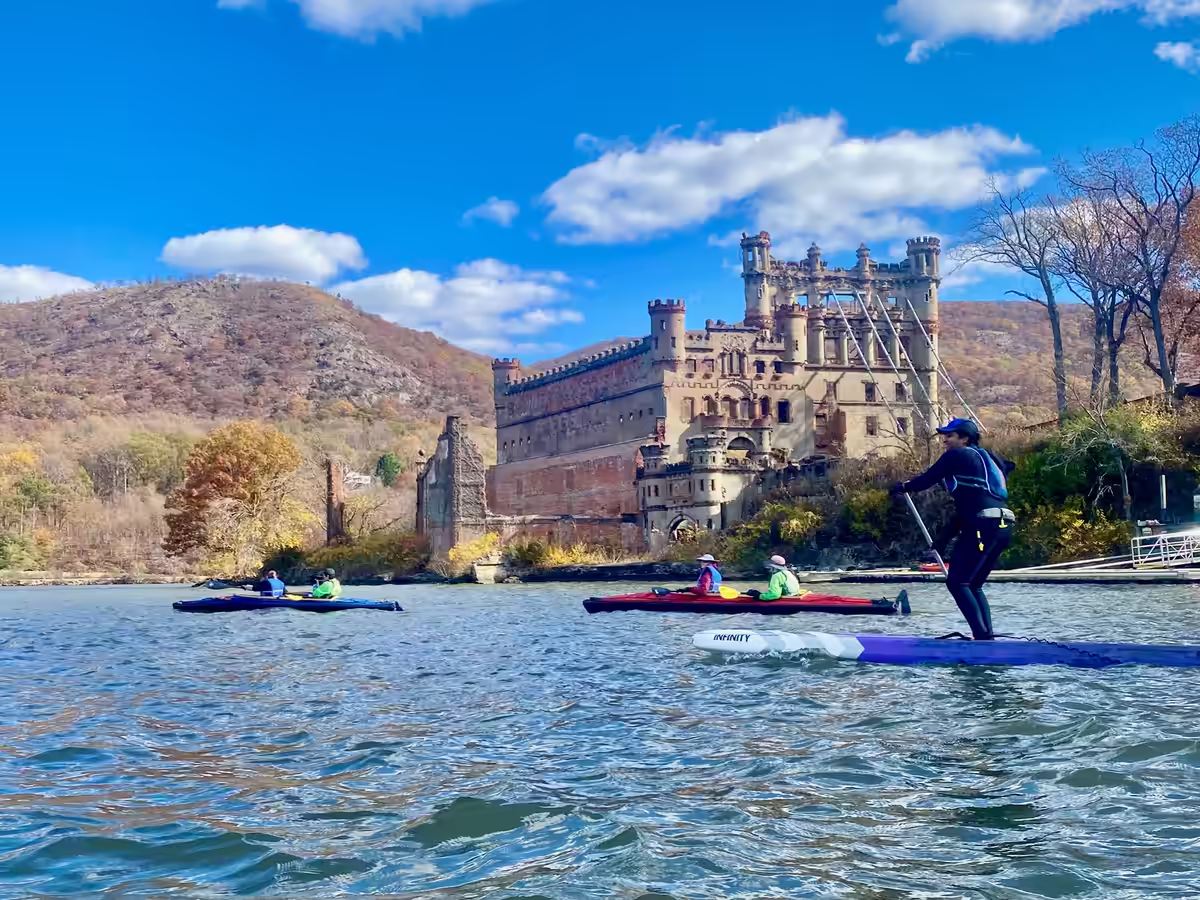 A paddleboarder and two tandem kayaks passing Bannerman Castle during the autumn in the Hudson Highlands.