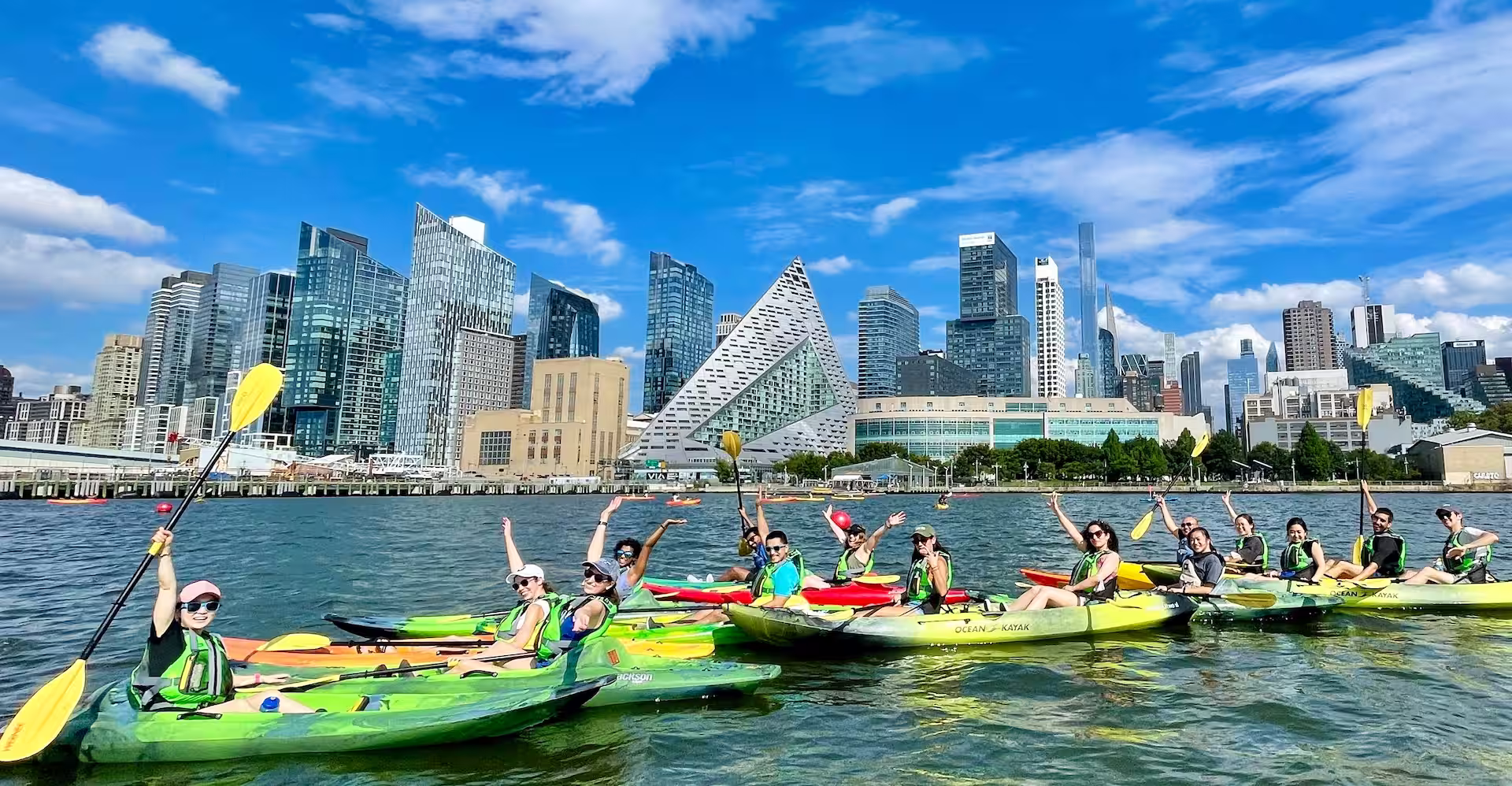 A diverse team of coworkers enjoying a private Hudson River kayak trip with panoramic views of the Midtown Manhattan skyline and Hudson Yards.