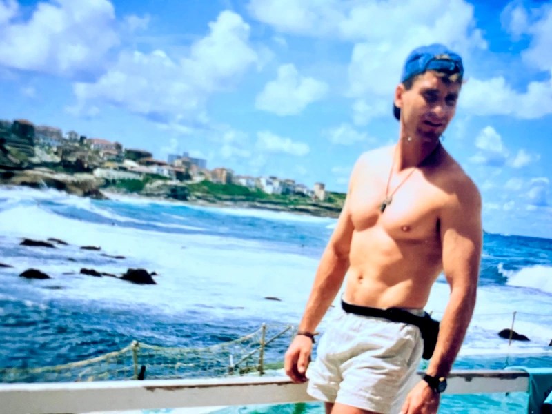 Man in shorts and cap by the ocean with a cloudy sky in the background.