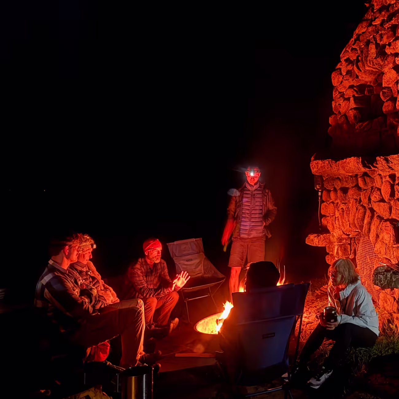 Group of people around a campfire at night near a stone structure.