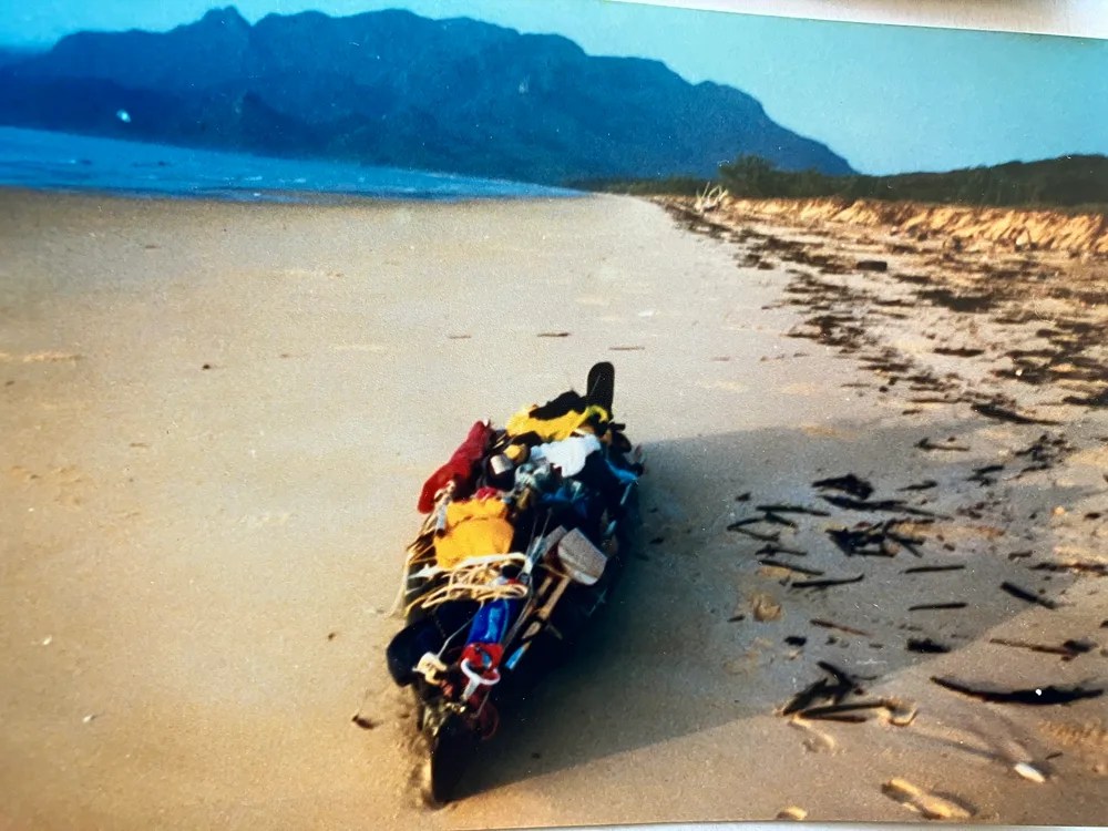 Loaded canoe on a sandy beach with mountains in the background.