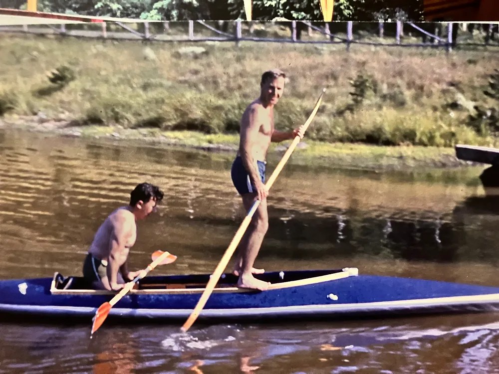 Two men on a paddleboard in a lake, both holding paddles.