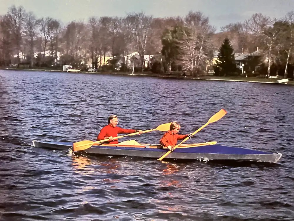 Two people kayaking on a calm lake surrounded by trees.