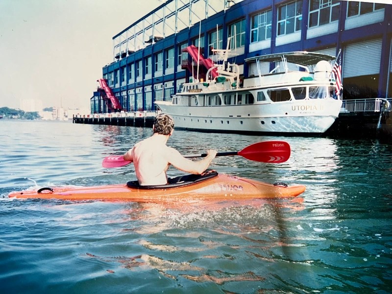 Person kayaking near a docked yacht and building with red slides.