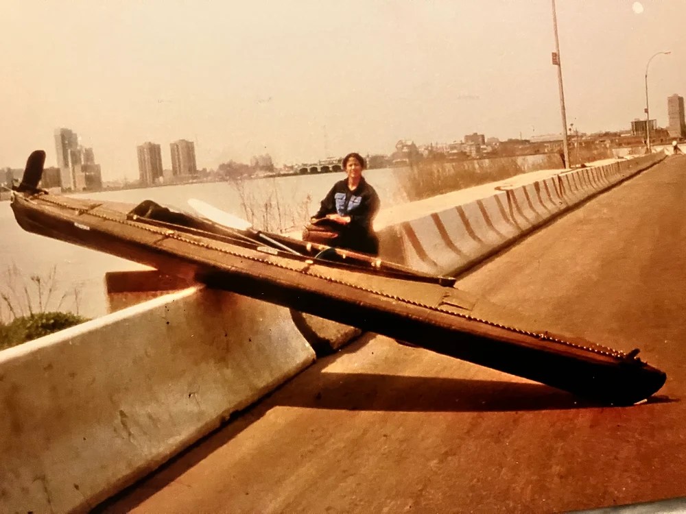 Person sitting on a wall beside a large metal beam on a highway barrier.