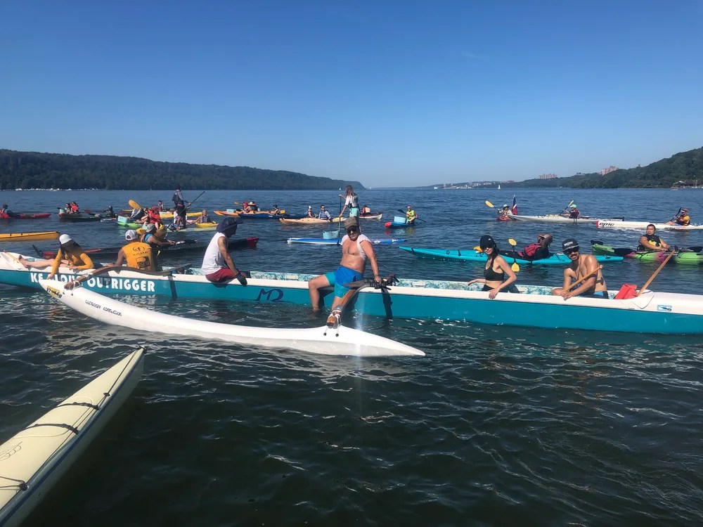People kayaking and canoeing on a sunny lake with green hills in the background.