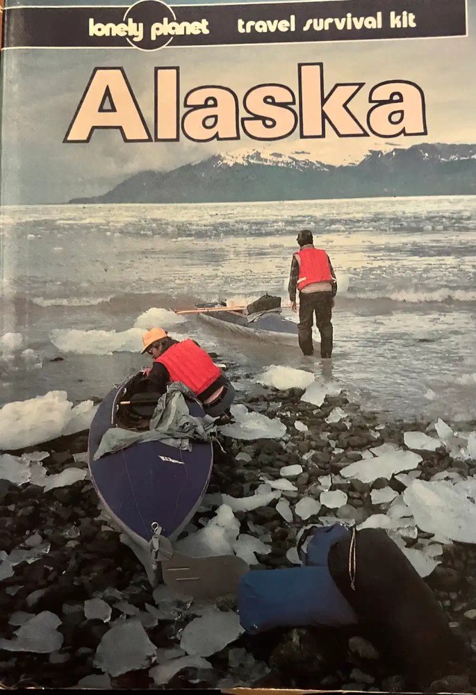Two people with kayaks on an icy shoreline in Alaska.