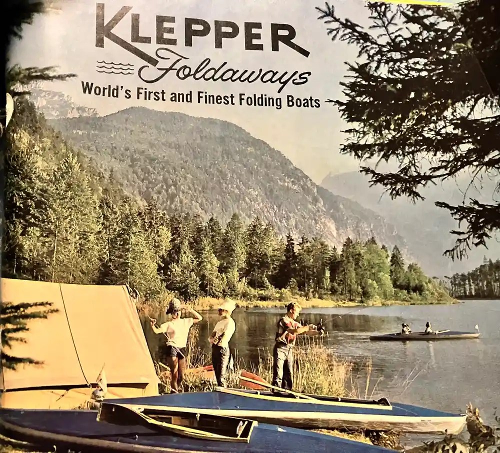 People near folding boats by a lake with mountains in the background.