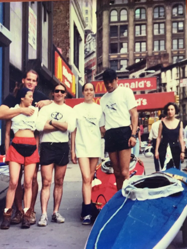Group of people in sportswear standing on a city street beside a kayak.
