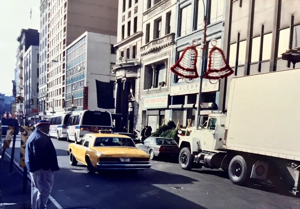 Busy urban street with cars, buses, and buildings featuring decorative red bell overlays.