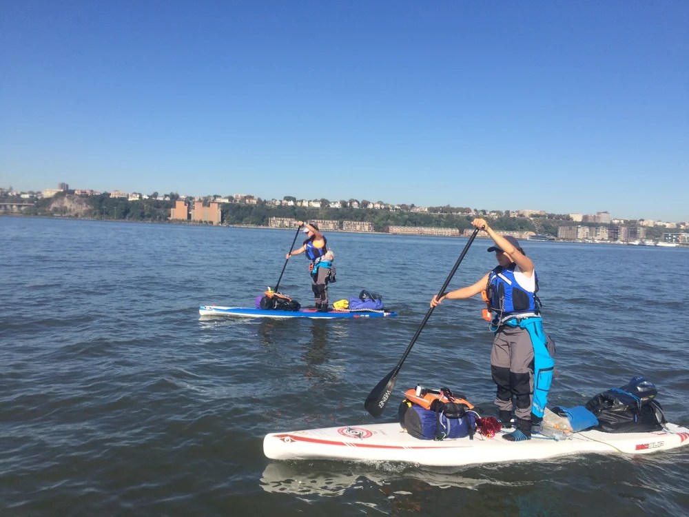 Two people paddleboarding on a lake with a cityscape in the background.