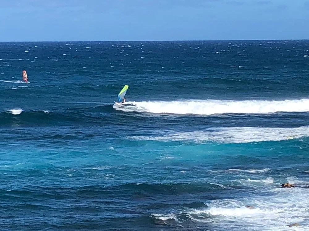 Windsurfers on the ocean with waves and a clear blue sky.