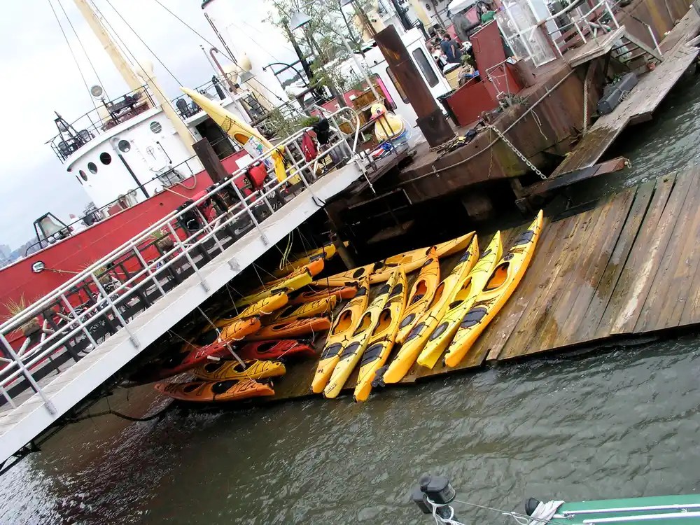 Yellow kayaks stacked near a docked red ship.