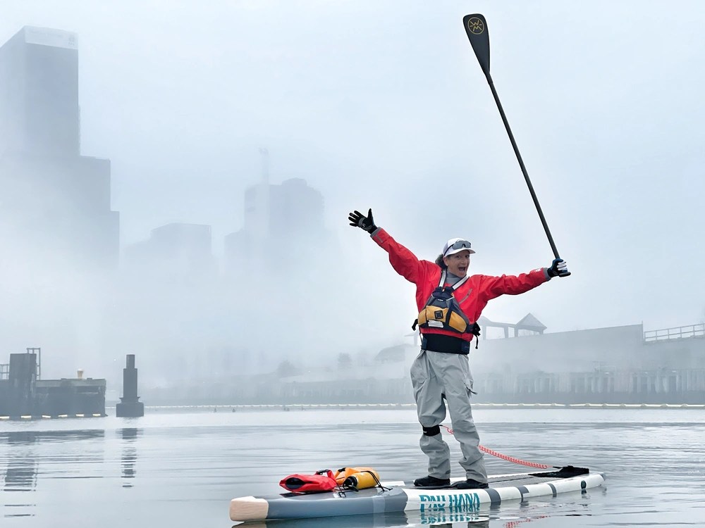 Stephanie Jackenthal paddling on foggy water, arms raised, wearing red jacket and life vest.
